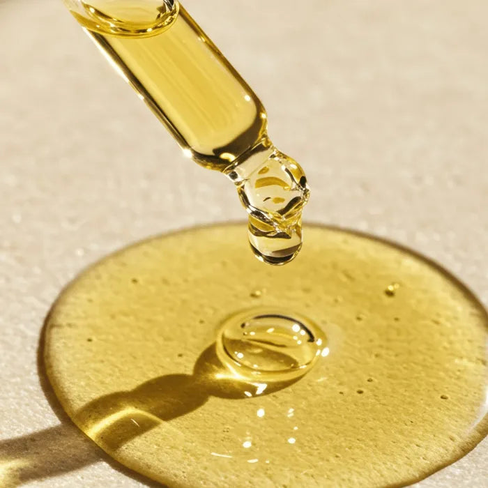 Goldgelbes Hautöl tropft aus einer Glaspipette auf eine helle Fläche und bildet eine runde Öllache