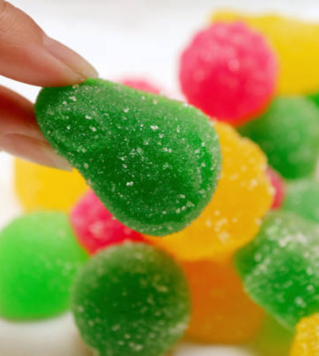 Hand wählt ein grünes CBD Gummibonbon aus einer bunten Auswahl, Nahaufnahme mit Fokus auf Süßigkeiten