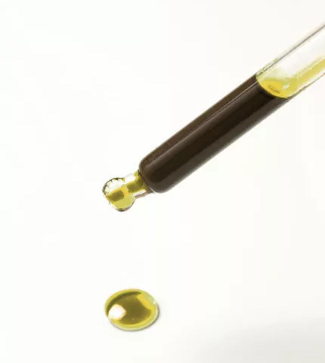 Nahaufnahme einer Pipette mit einem Tropfen goldenes CBD Öl, mit einem weiteren Tropfen darunter auf einem weißen Hintergrund, der die Reinheit und Konzentration des Öls hervorhebt.
