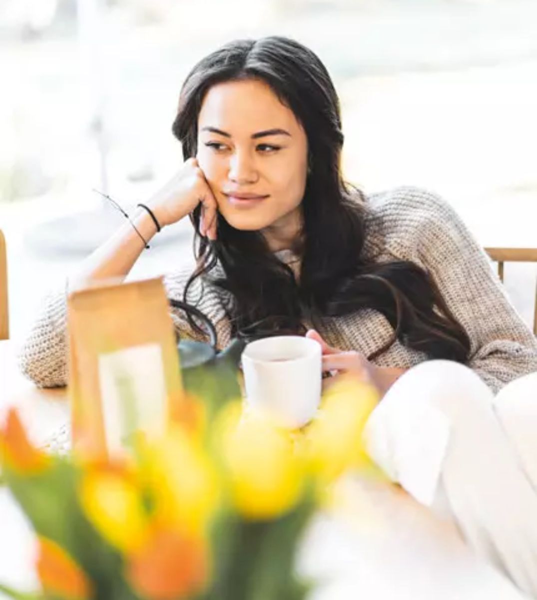 Glückliche Frau in einem Pullover hält eine Tasse Tee, genießt einen entspannenden Moment zu Hause