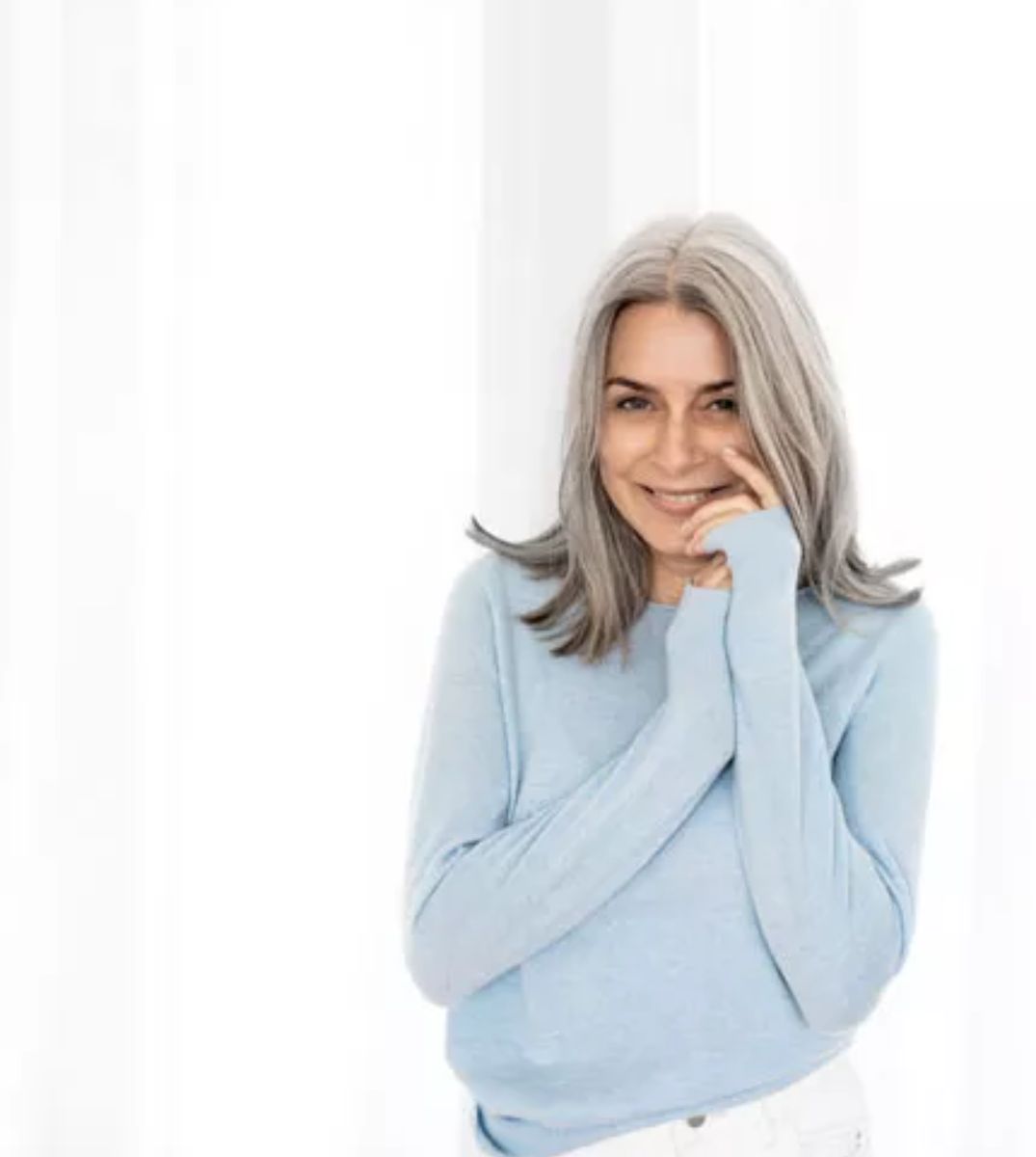Lächelnde reife Frau mit grauen Haaren in einem blauen Pullover, die Frische und Lebensfreude ausstrahlt