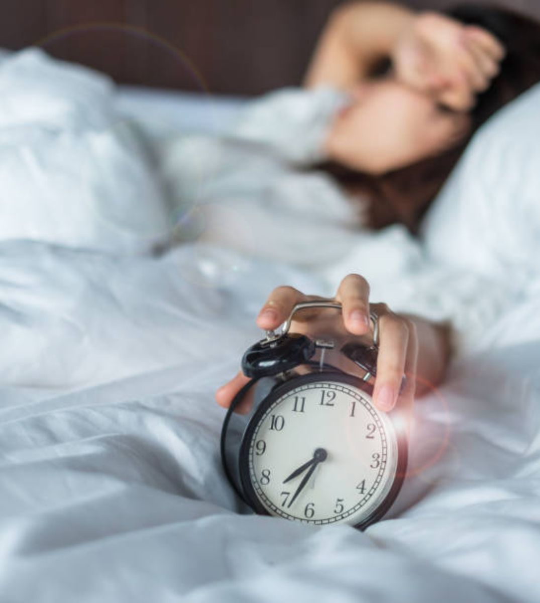 Frau im Bett schlägt den Schlummerknopf am Wecker, ein alltäglicher Moment des morgendlichen Aufwachens